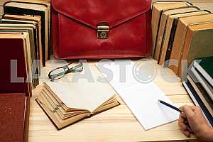 On a wooden table books, documents, calculator, red briefcase.