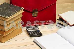 On a wooden table books, documents, calculator, red briefcase.