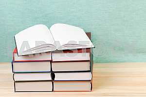Открытая книга, стопка книг в твердом переплете на деревянном столе. Обратно в школу. Копирование пространства