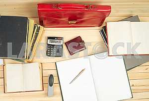 On a wooden table books, documents, calculator, red briefcase.