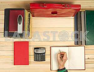On a wooden table books, documents, calculator, red briefcase.