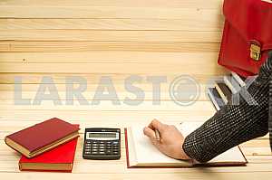 On a wooden table books, documents, calculator, red briefcase.