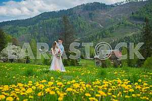 Wedding in mountains, A COUPLE IN LOVE, MOUNTAINS background, STANDING surounded dandelions, AMONG THE LAWN WITH THE GREEN GRASS, RUSTIC STYLE, GIRL IN LONG TULLE DRESS, romantic landscape