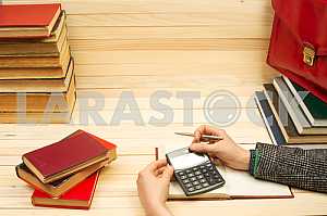 On a wooden table books, documents, calculator, red briefcase.