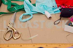 Scissors, reel of thread, measuring tapes and natural fabric. Sewing textile or cloth. Work table of a tailor. Textile tools. Copy space. Top view