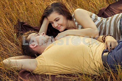 Young fashion beautiful loving casual style couple  lying down on floral field in autumnal park, warm sunny day, enjoying family, romantic date, happiness and love concept.