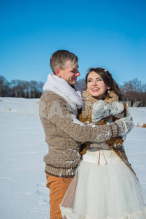 Young wedding couple holding each other on a sunny winter day. Rustic style wedding. lovely girl in short wedding white dress, blue sky on the background. Brown style wedding
