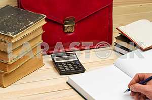 On a wooden table books, documents, calculator, red briefcase.