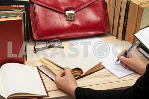On a wooden table books, documents, calculator, red briefcase.