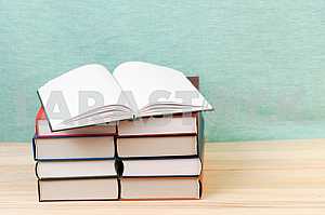 Открытая книга, стопка книг в твердом переплете на деревянном столе. Обратно в школу. Копирование пространства
