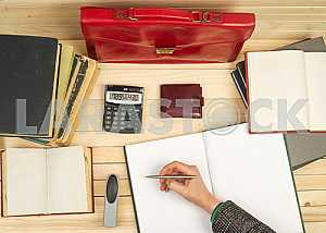 On a wooden table books, documents, calculator, red briefcase.