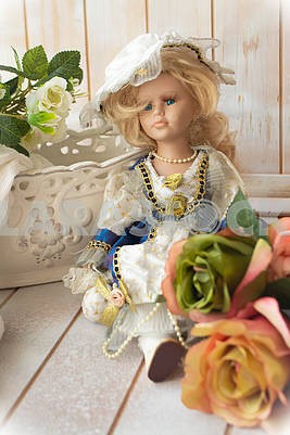 Vintage porcelain doll in victorian style. Doll with clothes and pastel roses. Vertical image, shabby background