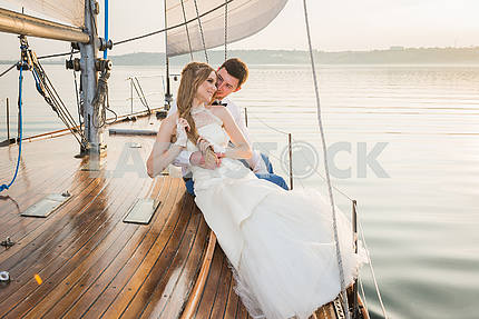 Happy bride and groom hugging on a yacht - looking into each other evening yellow sun