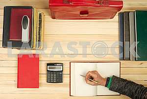 On a wooden table books, documents, calculator, red briefcase.
