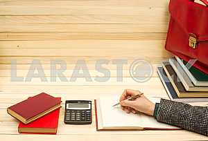On a wooden table books, documents, calculator, red briefcase.