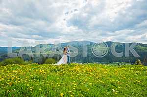 Wedding in mountains, A COUPLE IN LOVE, MOUNTAINS background, STANDING surounded dandelions, AMONG THE LAWN WITH THE GREEN GRASS, RUSTIC STYLE, GIRL IN LONG TULLE DRESS, romantic landscape