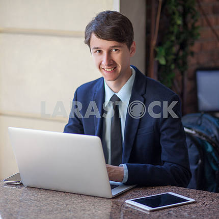 One relaxed young handsome professional businessman working with his laptop, phone and tablet in a noisy cafe. speak with phone.