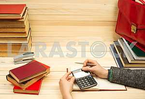 On a wooden table books, documents, calculator, red briefcase.