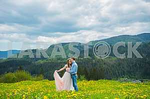 Wedding in mountains, a couple in love, mountains background, standing surrounded dandelions, among the lawn with the green grass, rustic style, girl in long tulle dress, romantic landscape