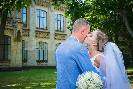Bride and groom, on the street, green tree and architecture building on the background, woman is kissing the man, wedding day