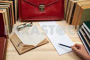 On a wooden table books, documents, calculator, red briefcase.
