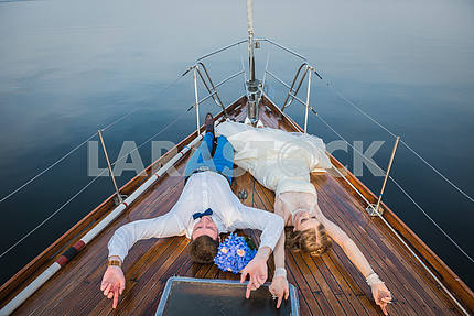 Счастливый медовый месяц парусный спорт - стильный молодой невесты и жениха, на деревянной доске парусной яхты - счастливо смотрят в небо