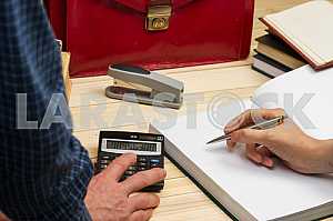 On a wooden table books, documents, calculator, red briefcase.