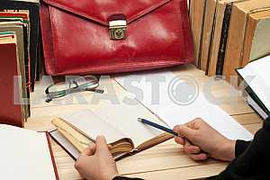 On a wooden table books, documents, calculator, red briefcase.