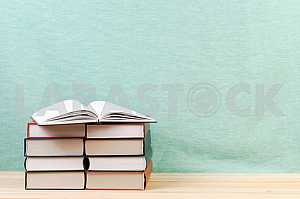 Открытая книга, стопка книг в твердом переплете на деревянном столе. Обратно в школу. Копирование пространства