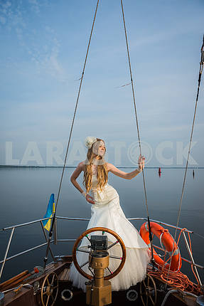 wedding on the sailing yacht . happy bride near the steering wheel, beautiful blonde in wedding dress. blue sky