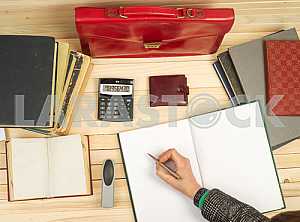 On a wooden table books, documents, calculator, red briefcase.