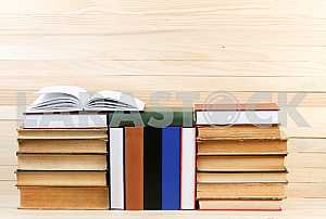 Открытая книга, стопка книг в твердом переплете на деревянном столе. Обратно в школу. Копирование пространства