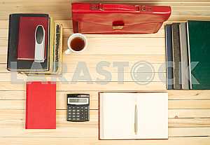 On a wooden table books, documents, calculator, red briefcase.
