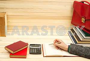 On a wooden table books, documents, calculator, red briefcase.