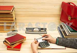 On a wooden table books, documents, calculator, red briefcase.