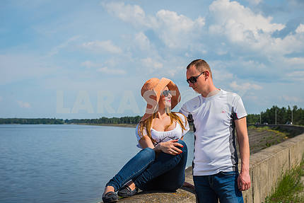 a love story couple travelling, resting near the water, looking into each other, on the sunny day, weared on jeans, blue sky and white clouds on the background