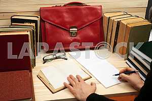 On a wooden table books, documents, calculator, red briefcase.