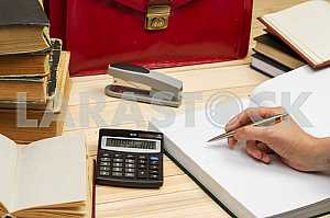 On a wooden table books, documents, calculator, red briefcase.