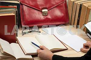 On a wooden table books, documents, calculator, red briefcase.