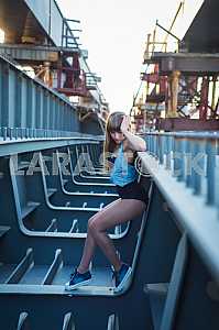 Woman standing sexy on the unfinished bridge, showing her legs, sporty, long hair, looking down