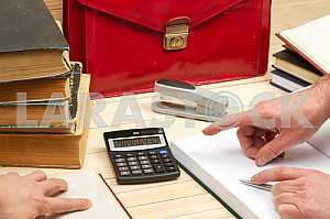 On a wooden table books, documents, calculator, red briefcase.