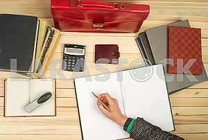 On a wooden table books, documents, calculator, red briefcase.
